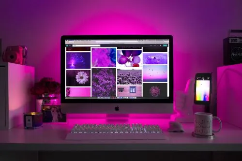 An iMac on a designer’s desk showing a mood board of colourful images, lit in pink