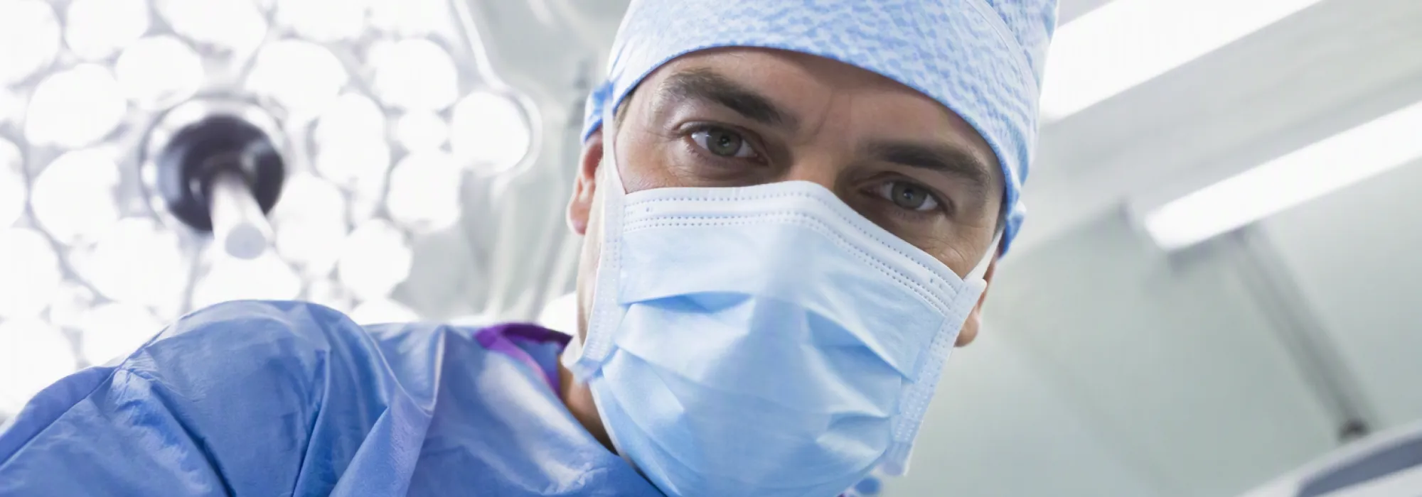 A surgeon in a blue cap, mask and gown leaning in for a closer look, representing a free website health check